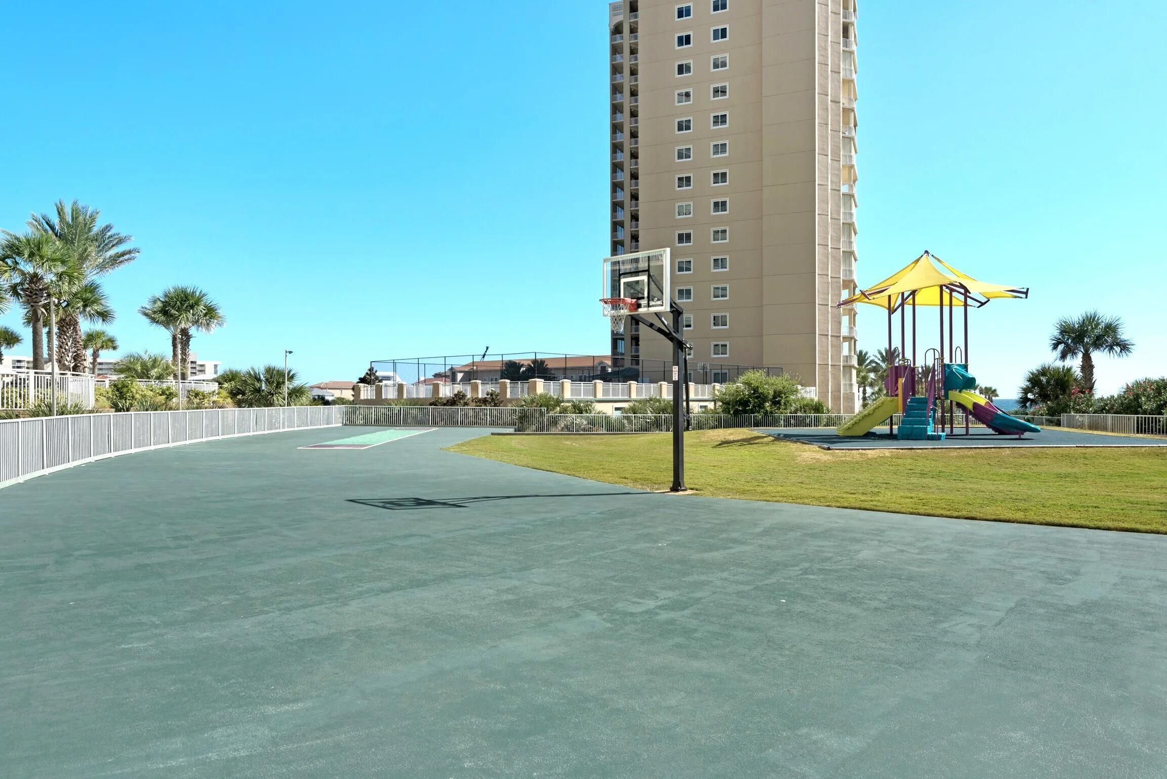 Una cancha de baloncesto con un parque infantil y un edificio alto al fondo.
