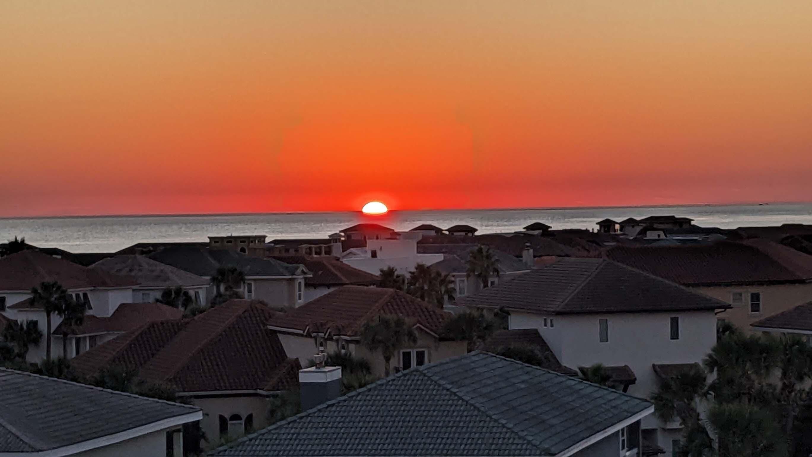 A coastal residential area with houses and a sunset over the ocean.