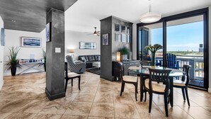 A spacious living area with a dining table and chairs, a sofa, and a balcony with a view. - Enclave 701b- Paradiso Del Regno (Destin)