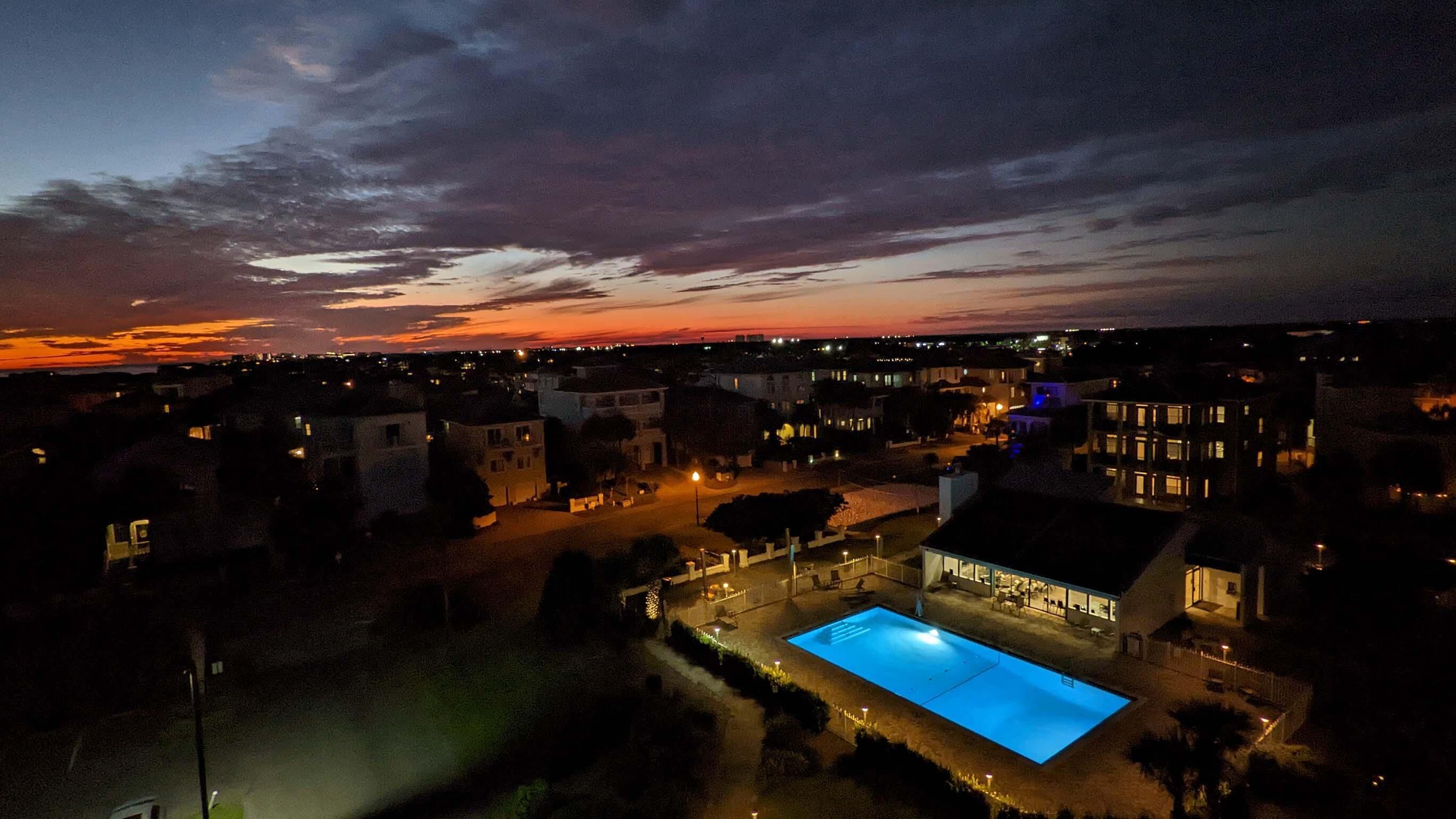 A residential area with a swimming pool, houses, and a sunset sky.