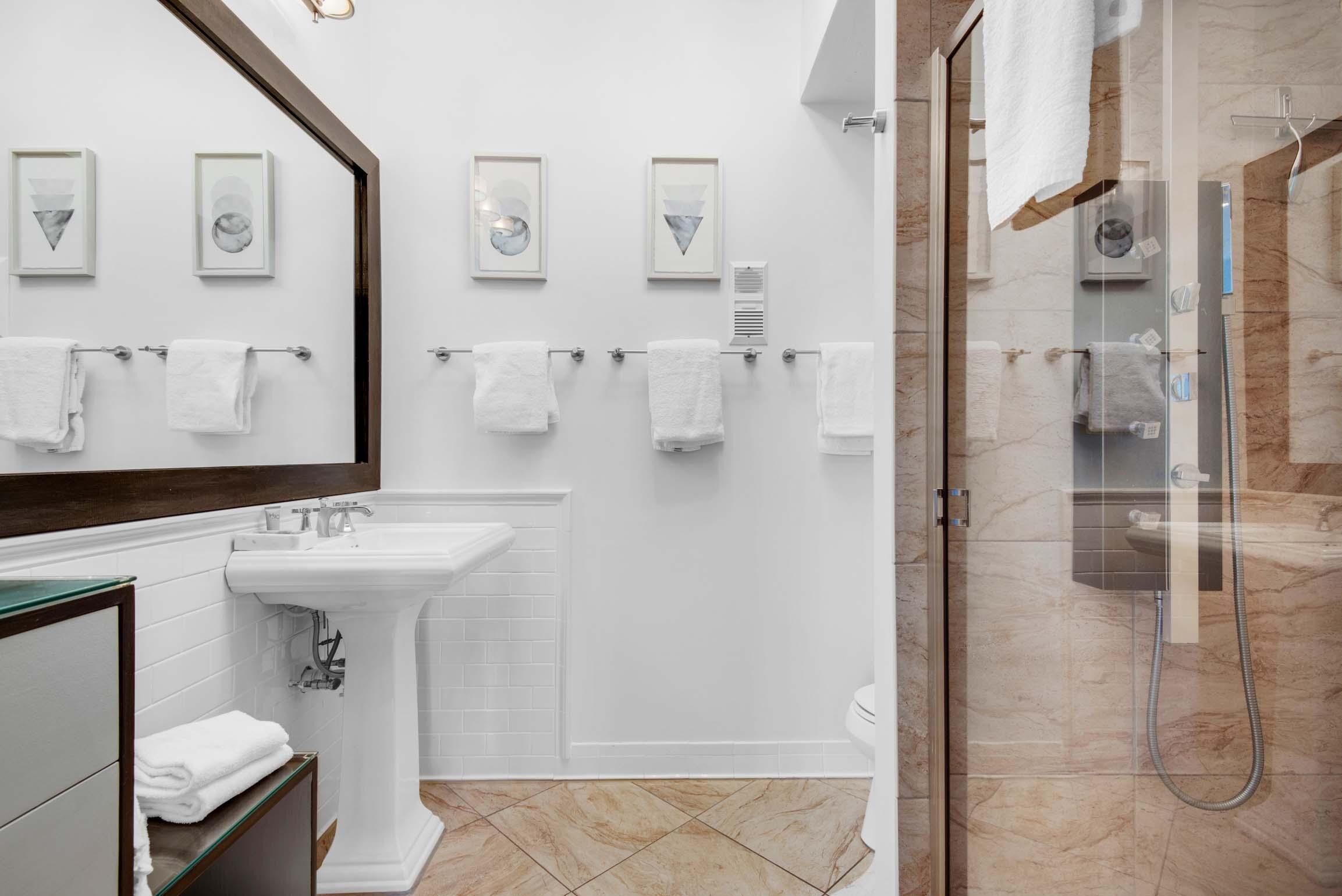 A modern bathroom with a large mirror, white sink, and glass shower enclosure.