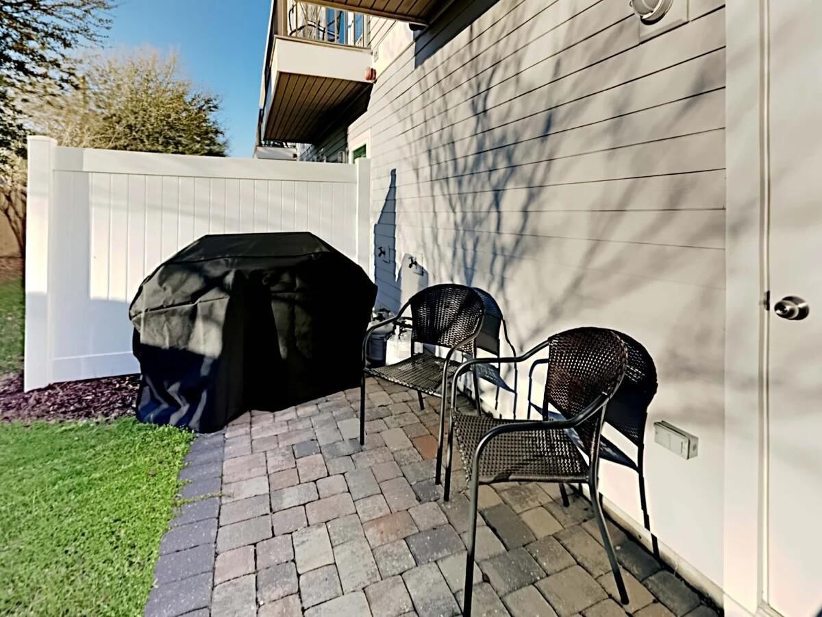 A patio area with a grill, two chairs, and a white fence.
