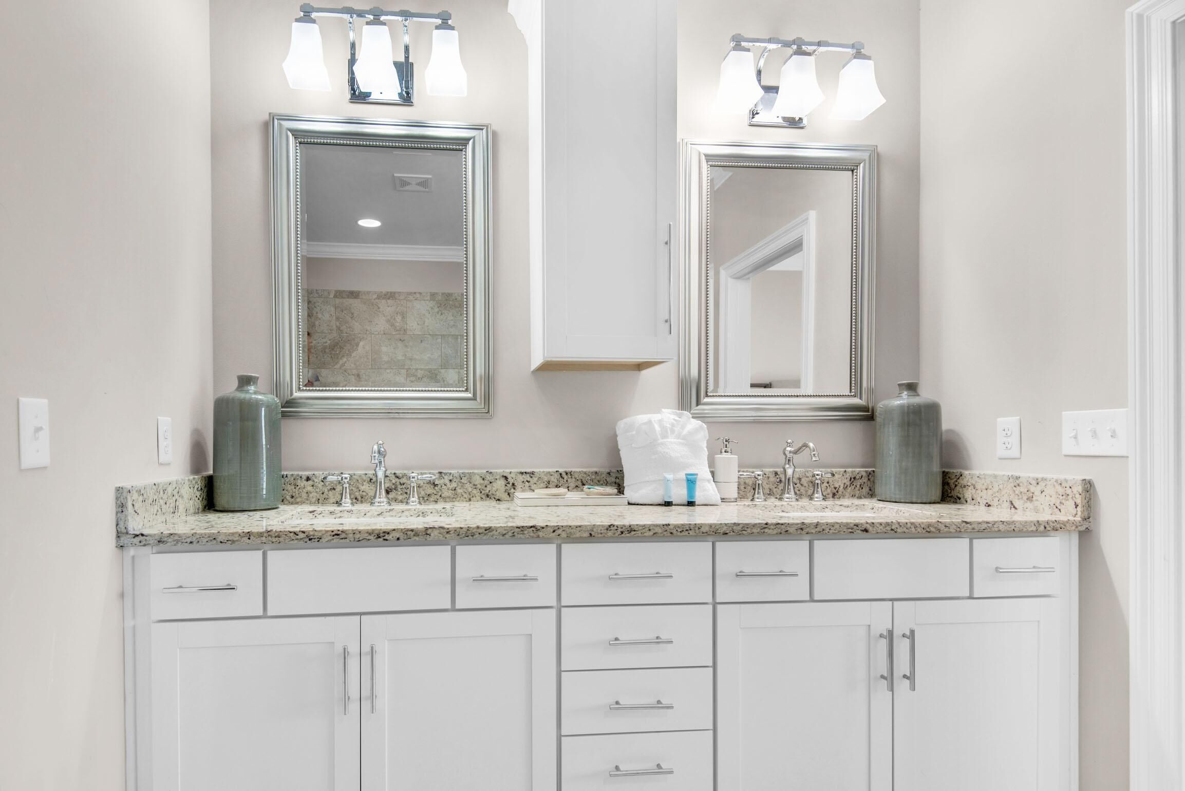 Un baño con dos espejos, encimera de granito y muebles de color blanco.
