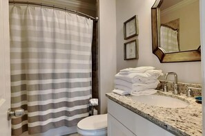 Une salle de bain avec un rideau de douche à rayures, un lavabo sur lequel sont pliées des serviettes et un miroir avec un cadre en bois.