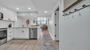 A modern kitchen with white cabinetry, a central island, and a view to the living area. - Dunes of Panama 203c (Panama City Beach)