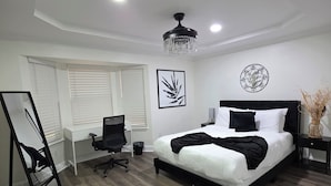 A bedroom with a bed, a desk, a chair, a standing lamp, and a ceiling fan.