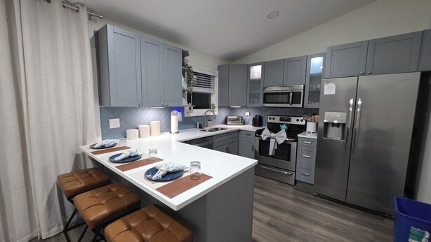 A modern kitchen with grey cabinets, a central island with stools, a microwave, oven, and a refrigerator.