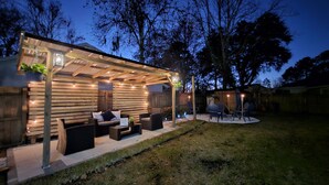 A covered patio area with seating and ambient lighting. - Lovely Home 10 min from Jax Airport w/Pool + Firepit. (Jacksonville)