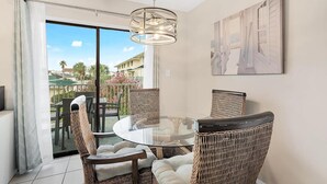 Un comedor con sillas de mimbre y una mesa de vidrio, una lámpara colgante y vistas a un balcón con mobiliario exterior.