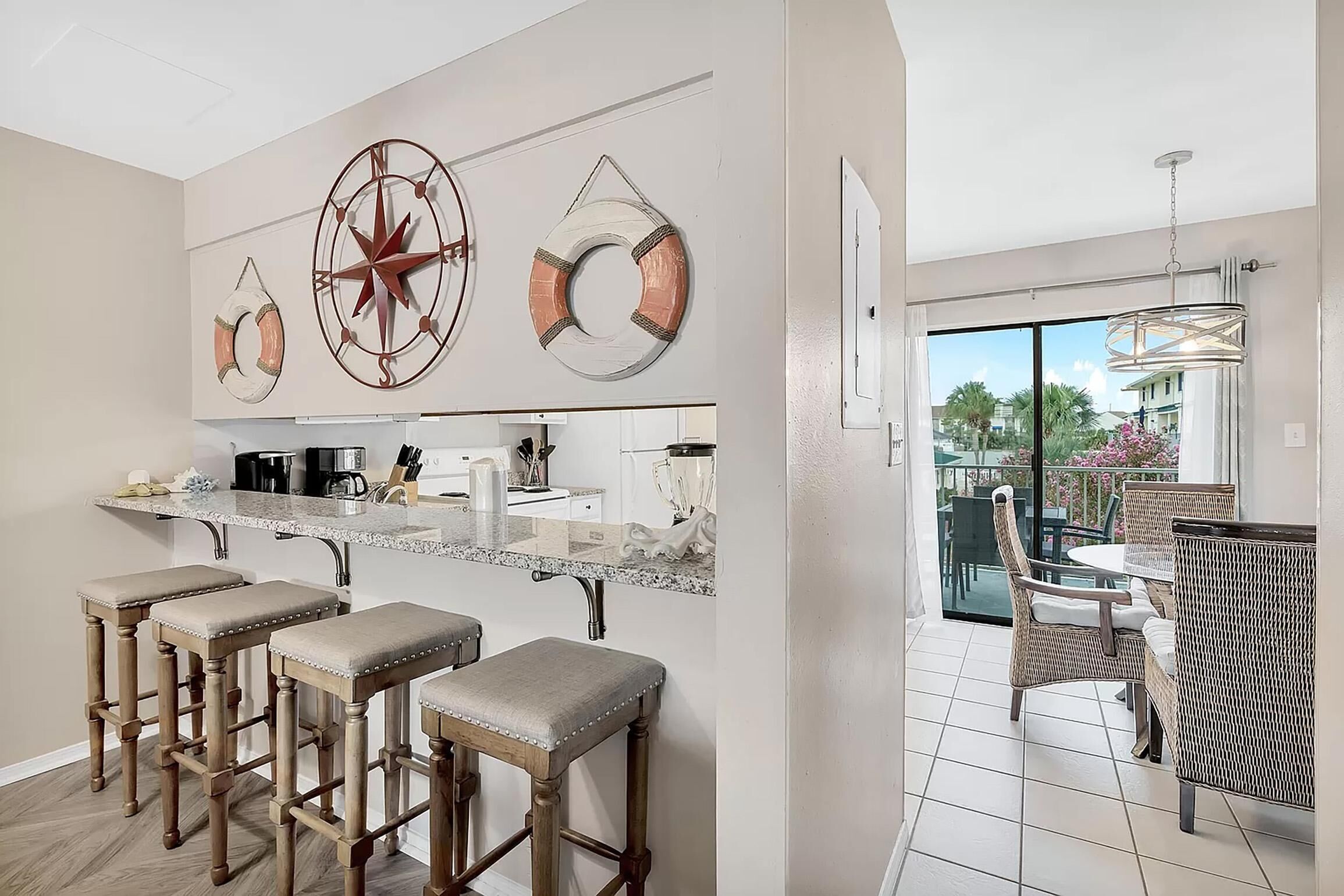 A modern kitchen with bar stools, a large window, and a dining area with wicker furniture.