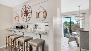 Una cocina moderna con taburetes de bar, un ventanal amplio y un comedor con mobiliario de mimbre.