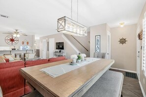 Un vaste espace de vie comprenant une longue table en bois, des canapés rouges et un ventilateur de plafond.