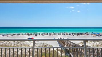 A beach view from a balcony with a wooden deck and a clear blue sky.