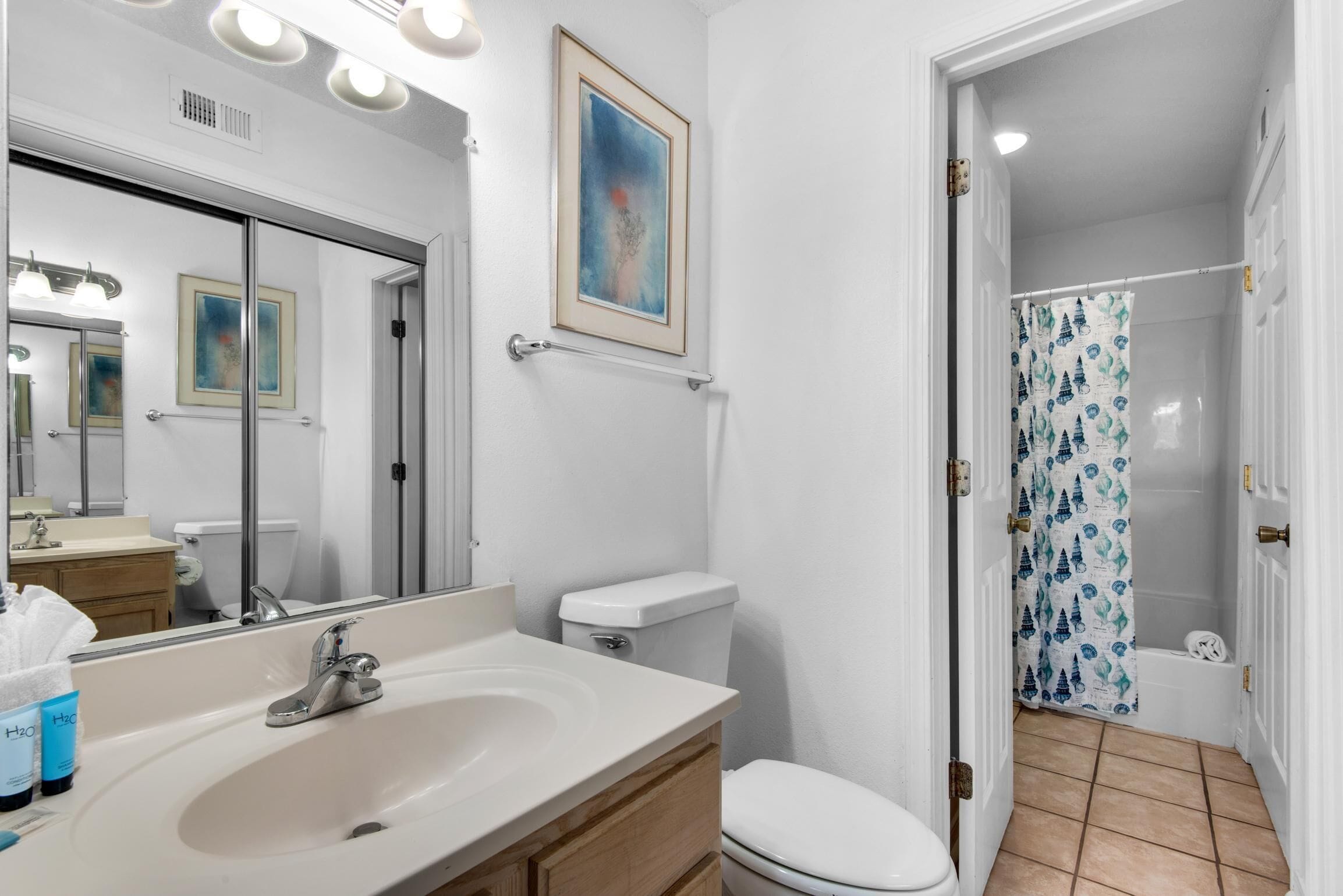 A bathroom with a sink, mirror, toilet, and shower curtain.