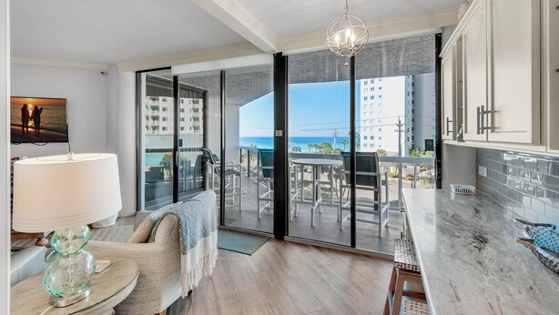 A modern living room with a large sliding glass door leading to a balcony with a city view. - Surfside Resort #208- Emerald Dreams (Miramar Beach)