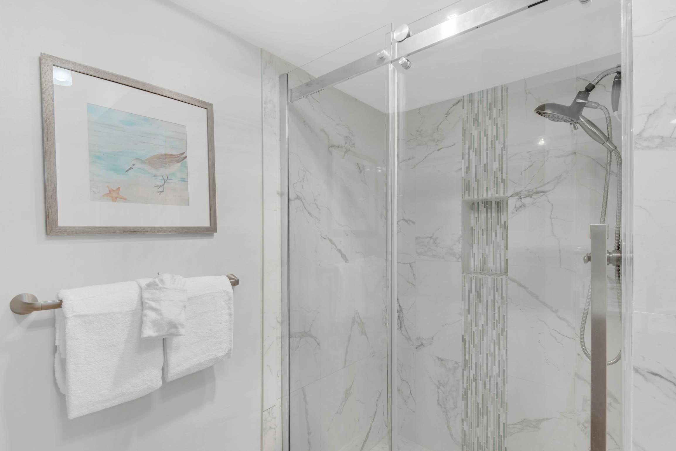 A bathroom with a glass shower enclosure, marble walls, and a framed picture of a bird on the wall.