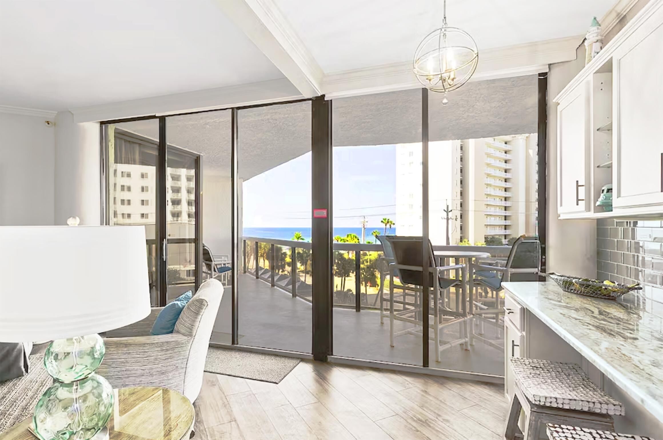 A modern living room with a large sliding glass door leading to a balcony with outdoor furniture and a view of the ocean.
