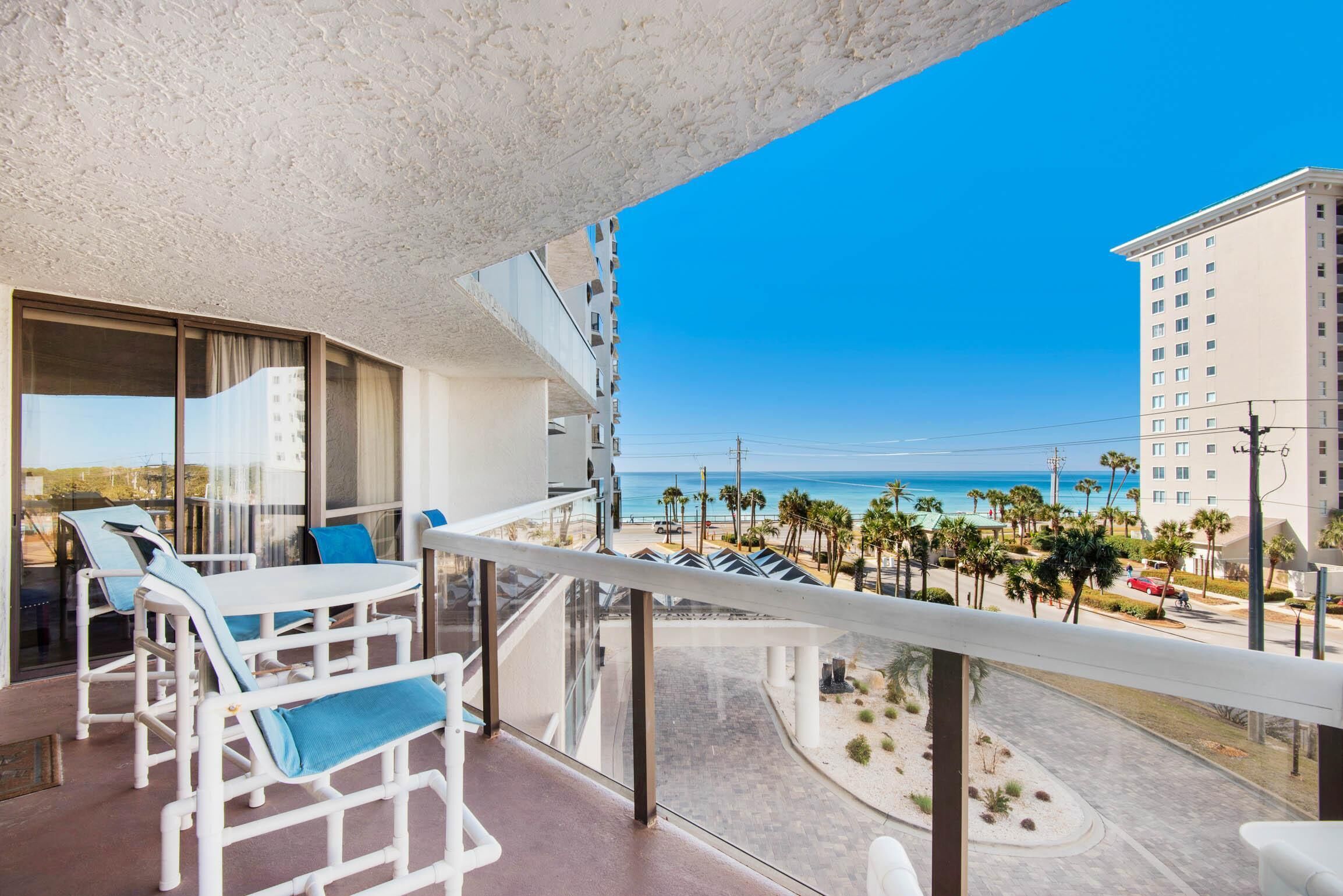 Un balcon avec une table et des chaises blanches, donnant sur une plage et des palmiers.