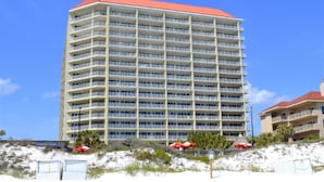 A multi-story hotel with a red roof, located on a sandy beach with palm trees and umbrellas. - Captiva 67 (Miramar Beach)