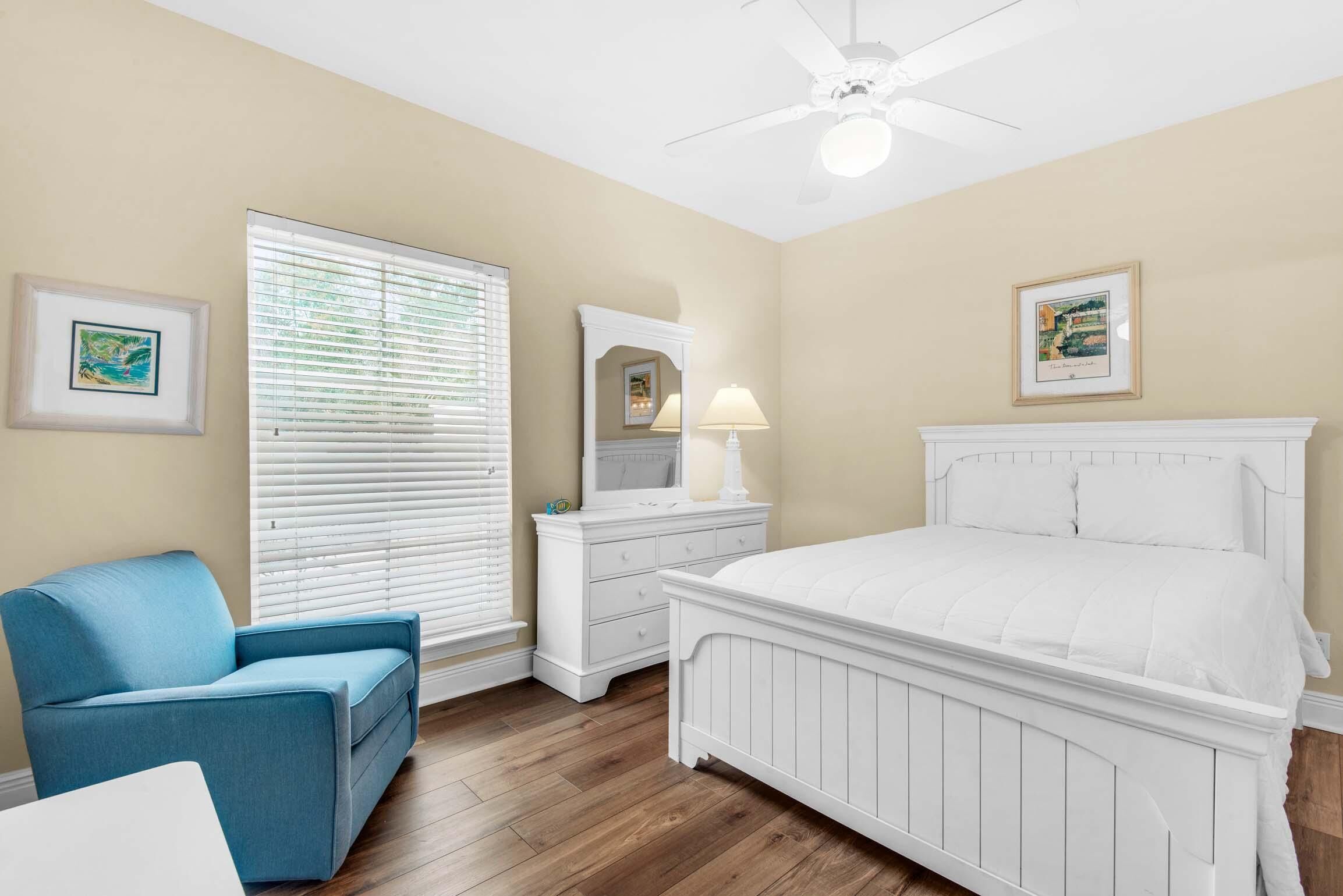 Une chambre à coucher avec un lit, une commode, une chaise et un ventilateur de plafond.