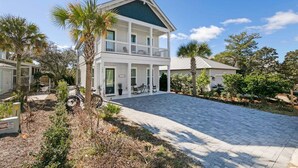 A two-story house with a balcony, a paved driveway, and surrounding palm trees. - Keeping It Reel on 30A (Santa Rosa Beach)