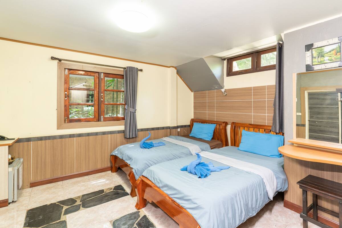 A hotel room with two wooden beds, a stone-tiled floor, a wooden bench, and a window with curtains.