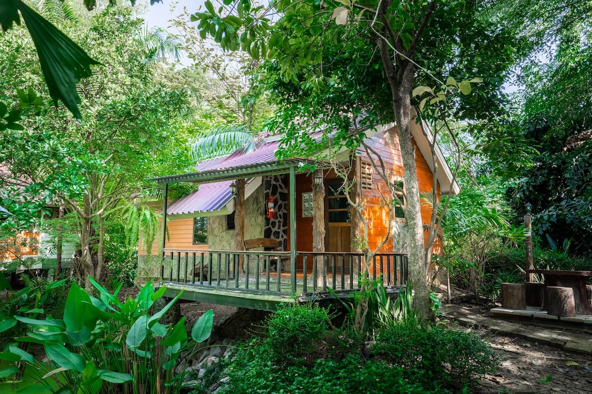 A treehouse with a wooden deck and a small porch, surrounded by lush greenery.