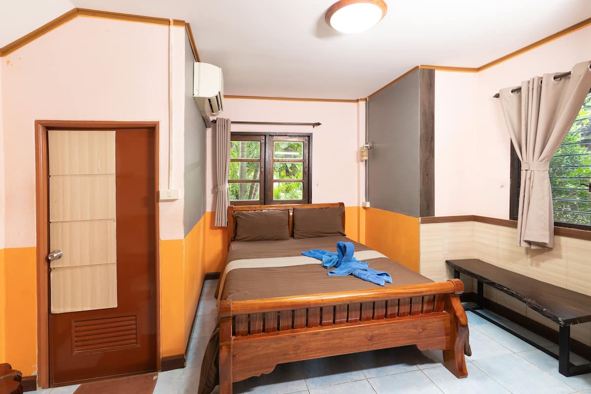A bedroom with a wooden bed, a bench, a window with curtains, and a door.