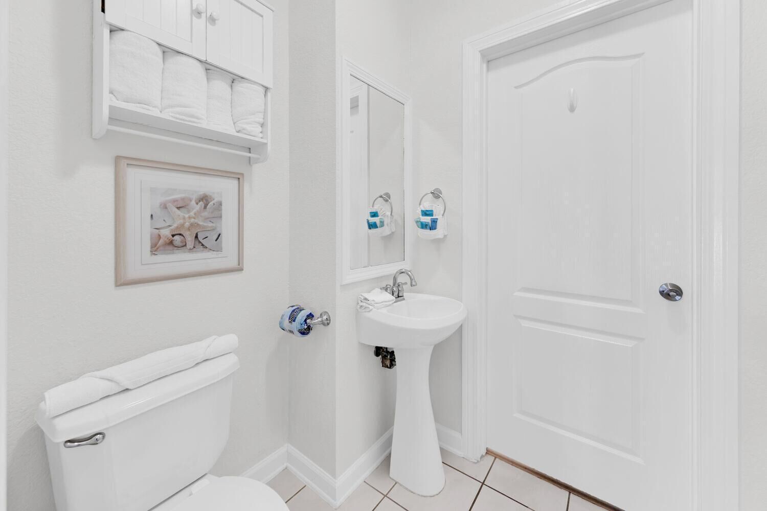 Une salle de bain comprenant des toilettes, un lavabo sur colonne, un miroir et une porte.