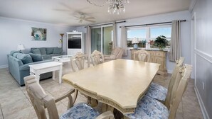 Un espace repas comprenant une grande table et des chaises, un canapé, un téléviseur et un ventilateur de plafond.