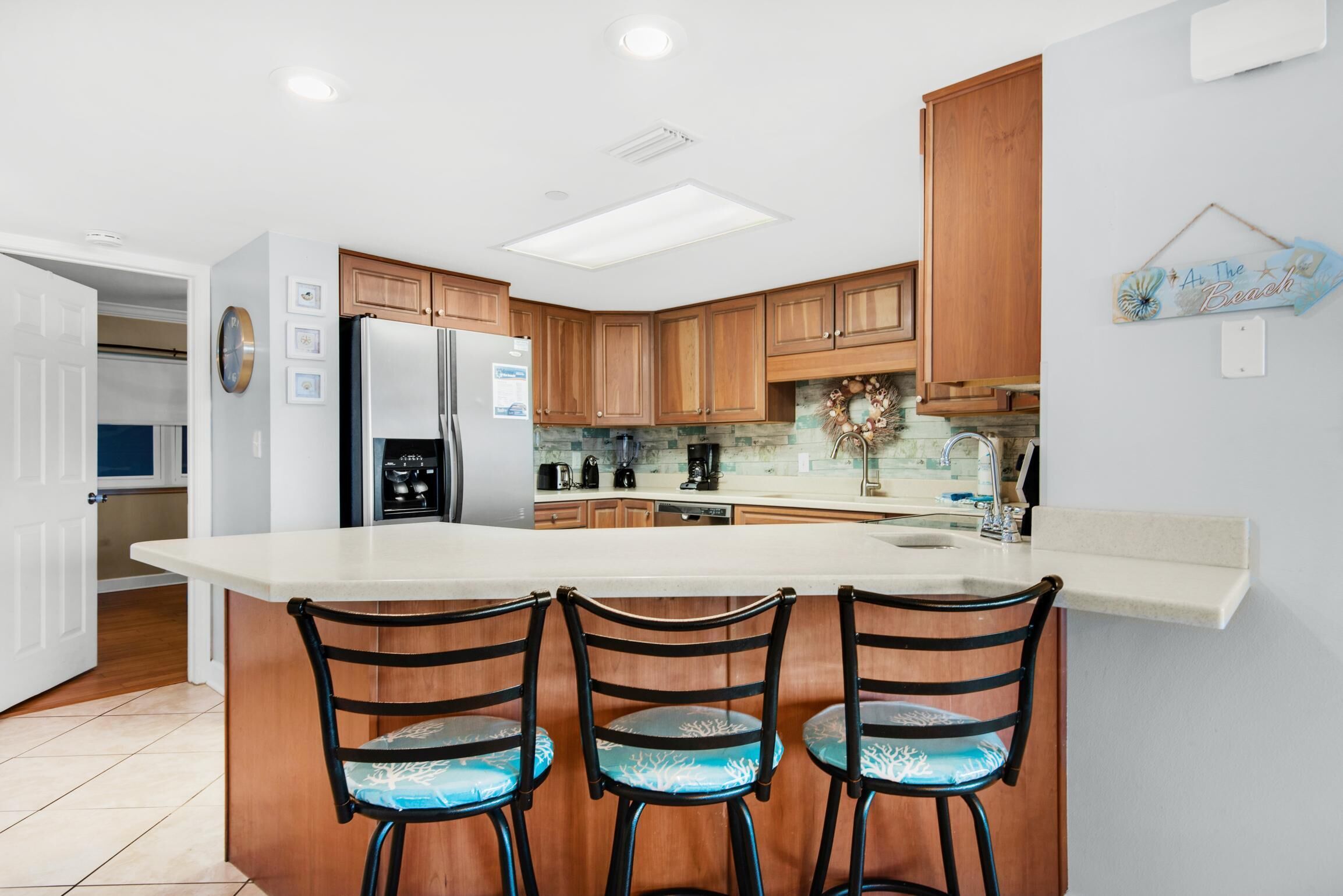 A modern kitchen with wooden cabinets, a large island with bar stools, and a decorative sign on the wall.