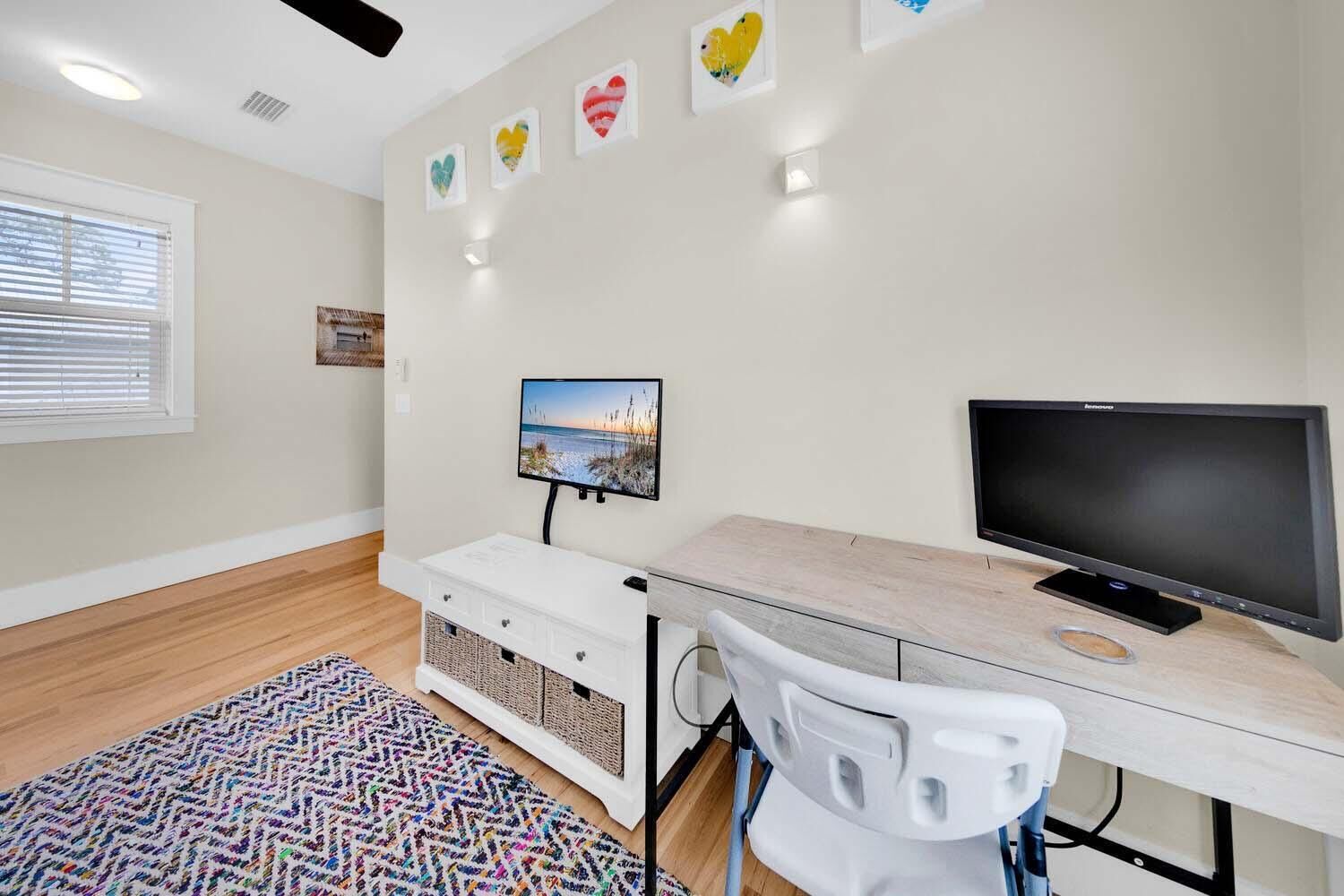 Una habitación moderna y bien iluminada con un escritorio de madera, un televisor y una alfombra colorida.