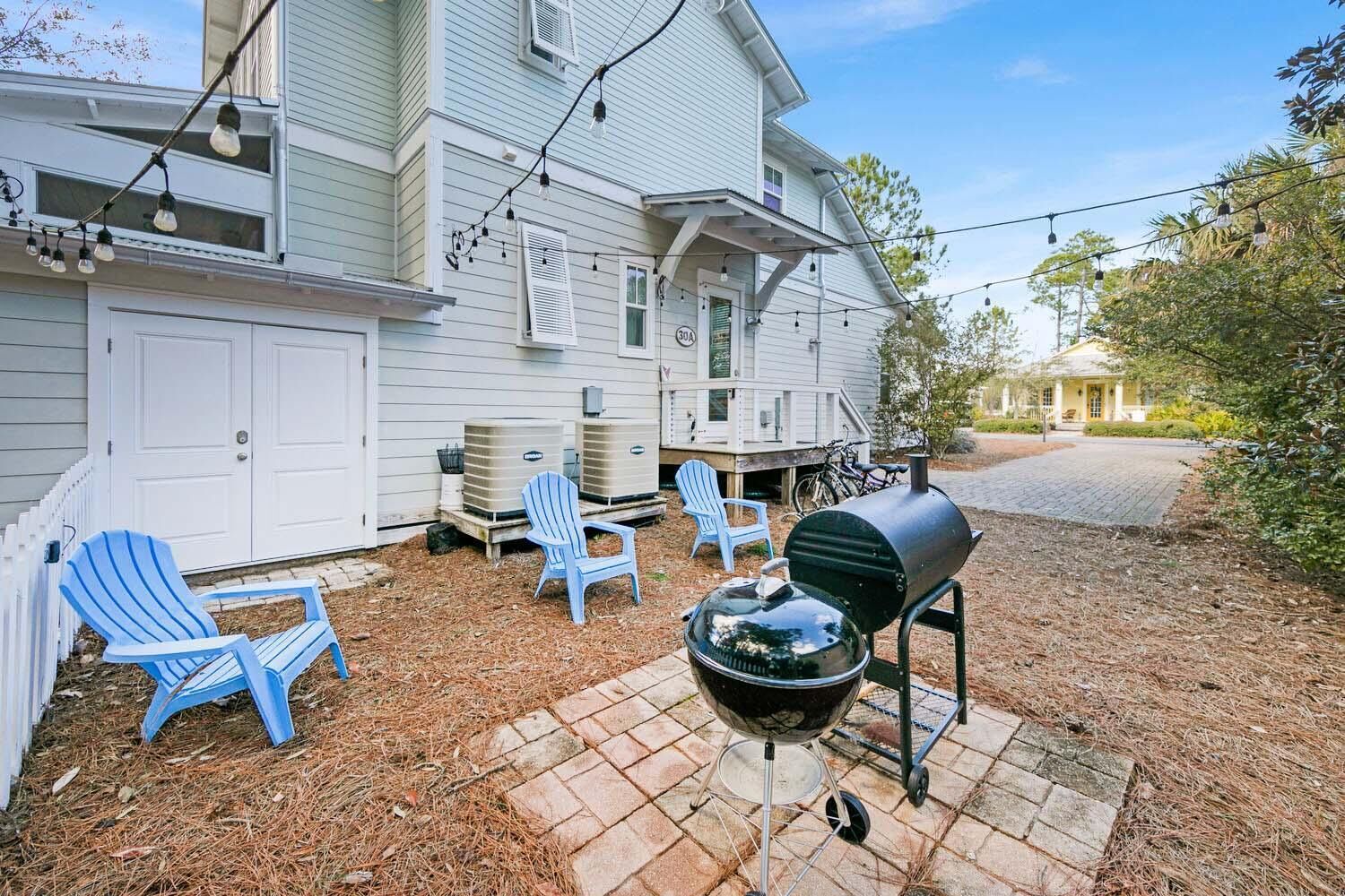 A backyard with a barbecue grill, two Adirondack chairs, and a white house.