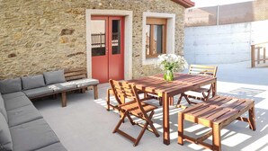 Un bâtiment en pierre avec une table et des bancs en bois, un canapé gris et une porte rouge.