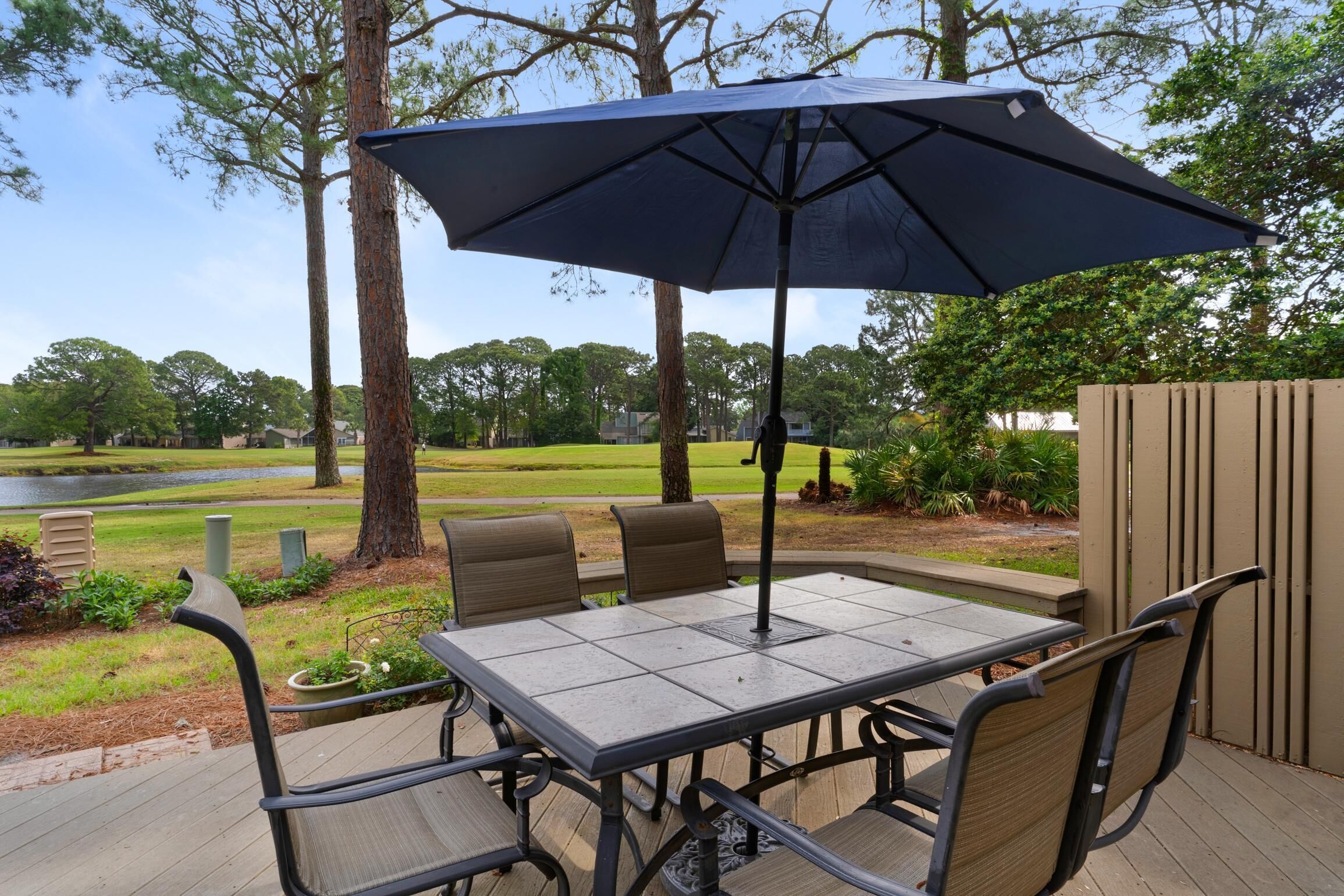 Une terrasse extérieure avec une table et des chaises, un grand parasol et une vue sur un lac et des arbres.