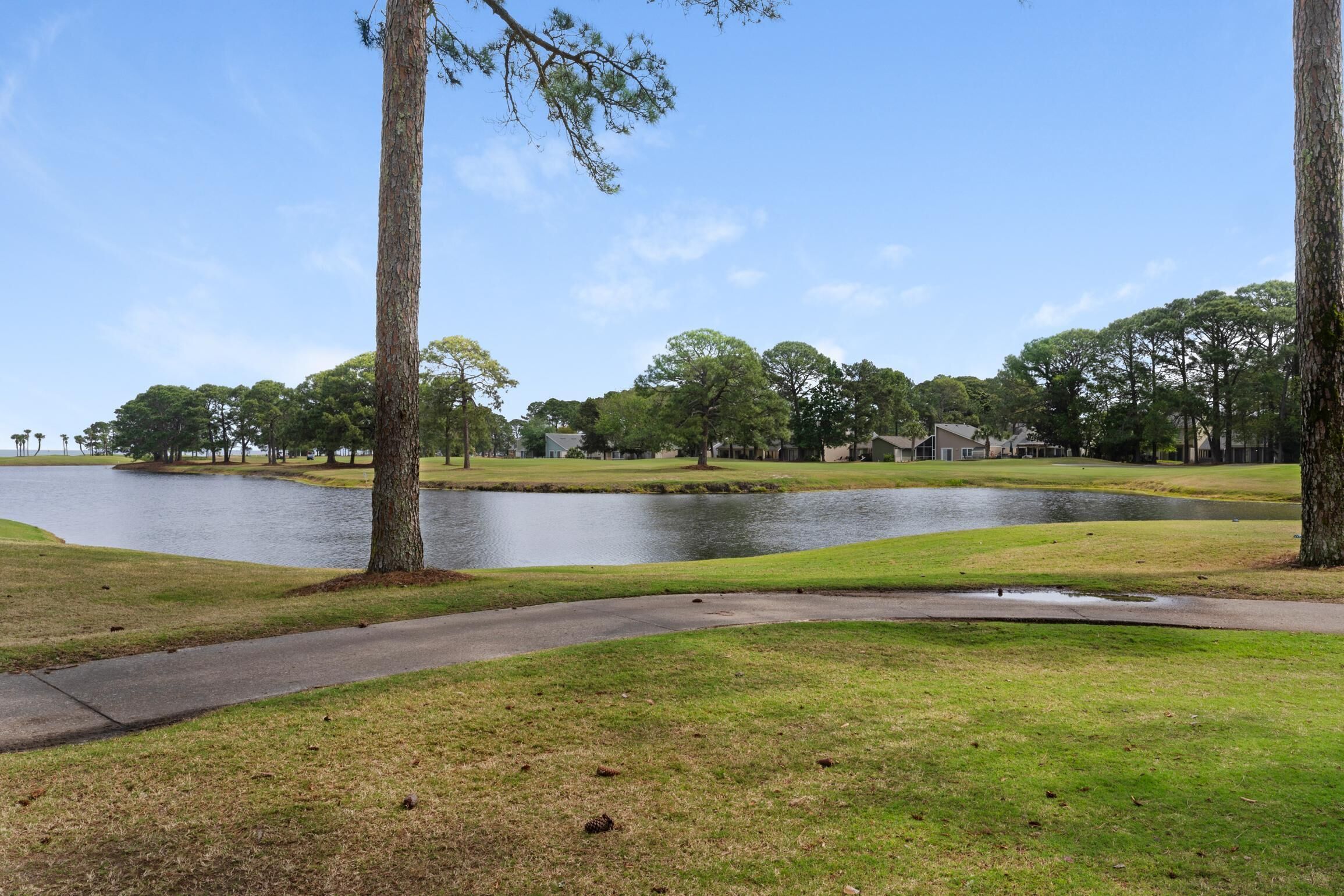 A golf course with a pond, trees, and a walking path.