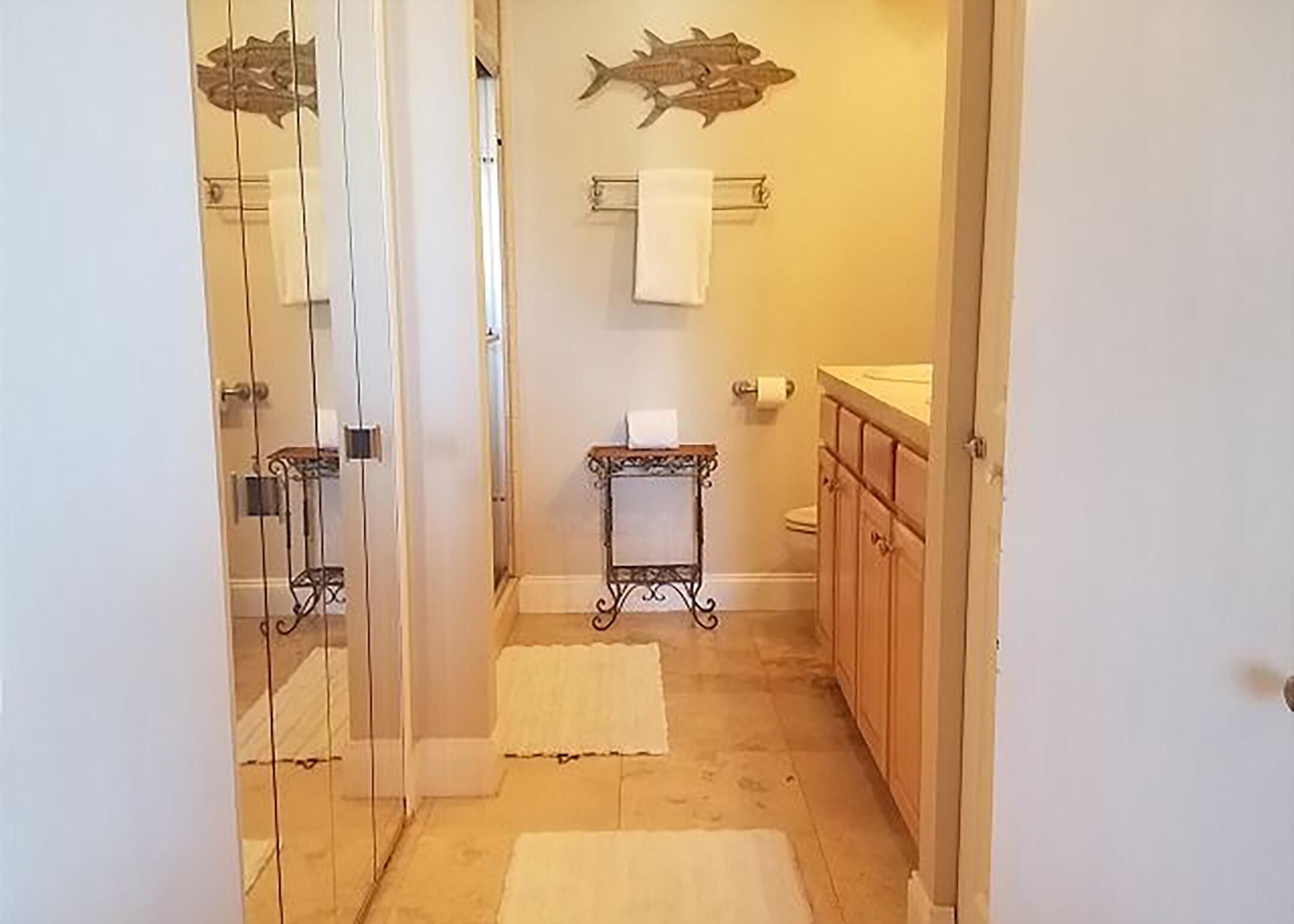 A narrow bathroom with a glass door, a wooden vanity, a toilet, and a towel rack.