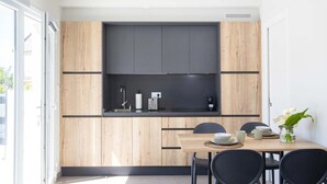 Una cocina moderna con estufa integrada, un lavamanos y una cafetera. Hay una mesa de comedor con sillas y un florero con flores.