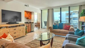 Ein modernes Wohnzimmer mit Flachbildfernseher, Holzschränken, einem Glastisch und einer Couch mit bunten Kissen.