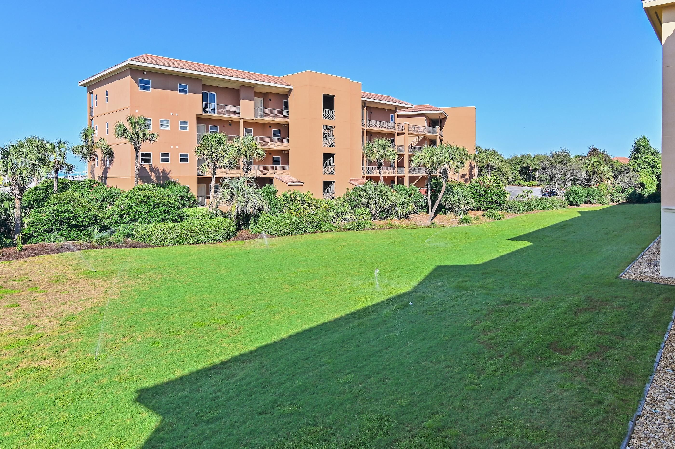 A multi-story building with balconies, surrounded by well-maintained lawns and palm trees.