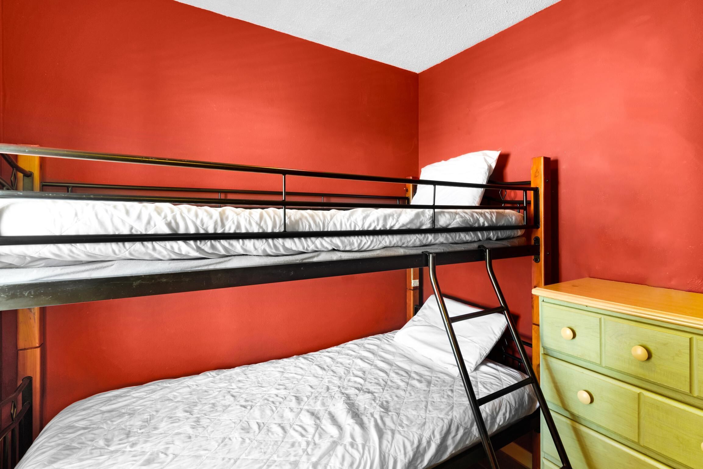 Une chambre avec un lit superposé, des murs rouges, une commode en bois et un matelas blanc.