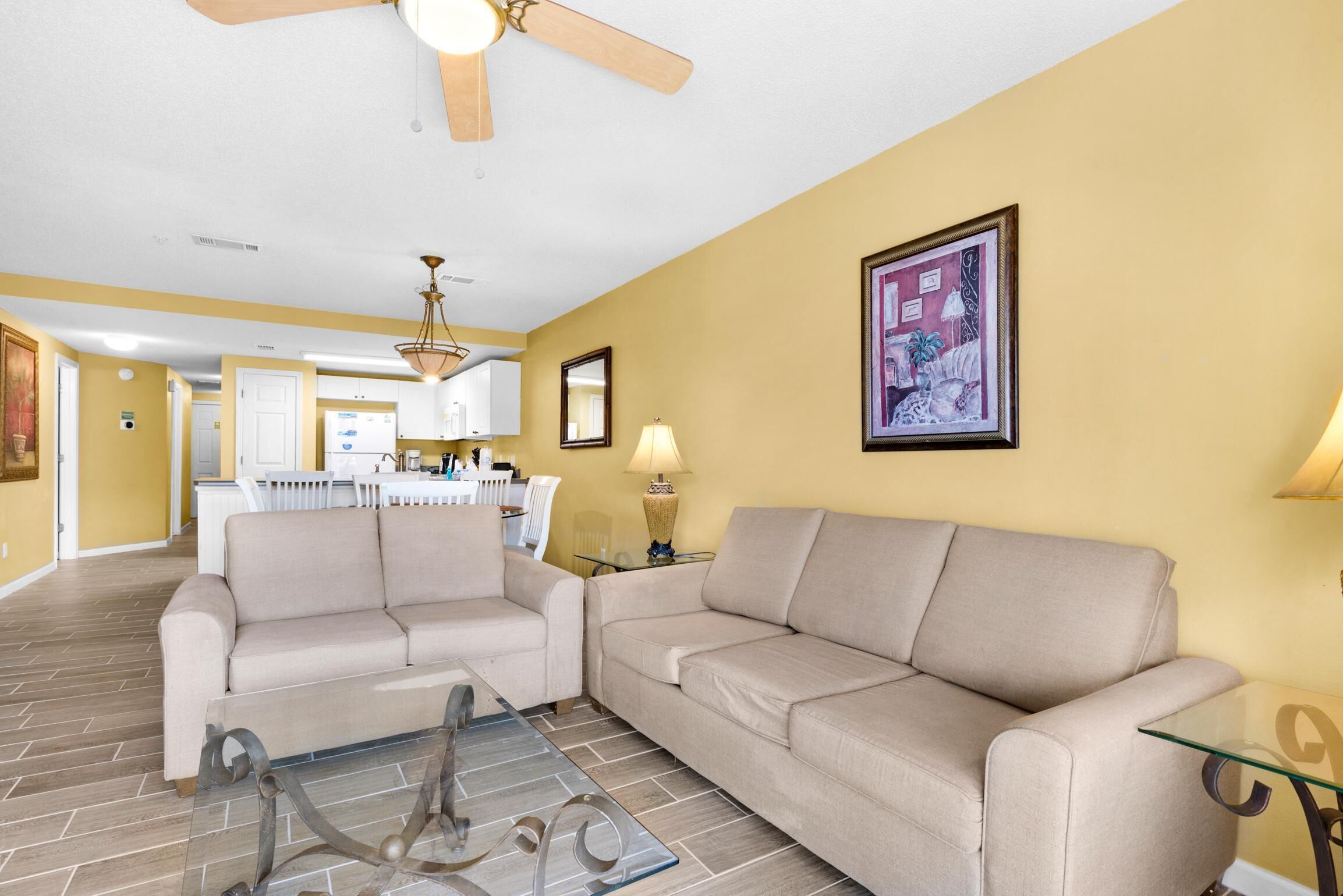 A living room with a beige sofa, a glass coffee table, and a ceiling fan.