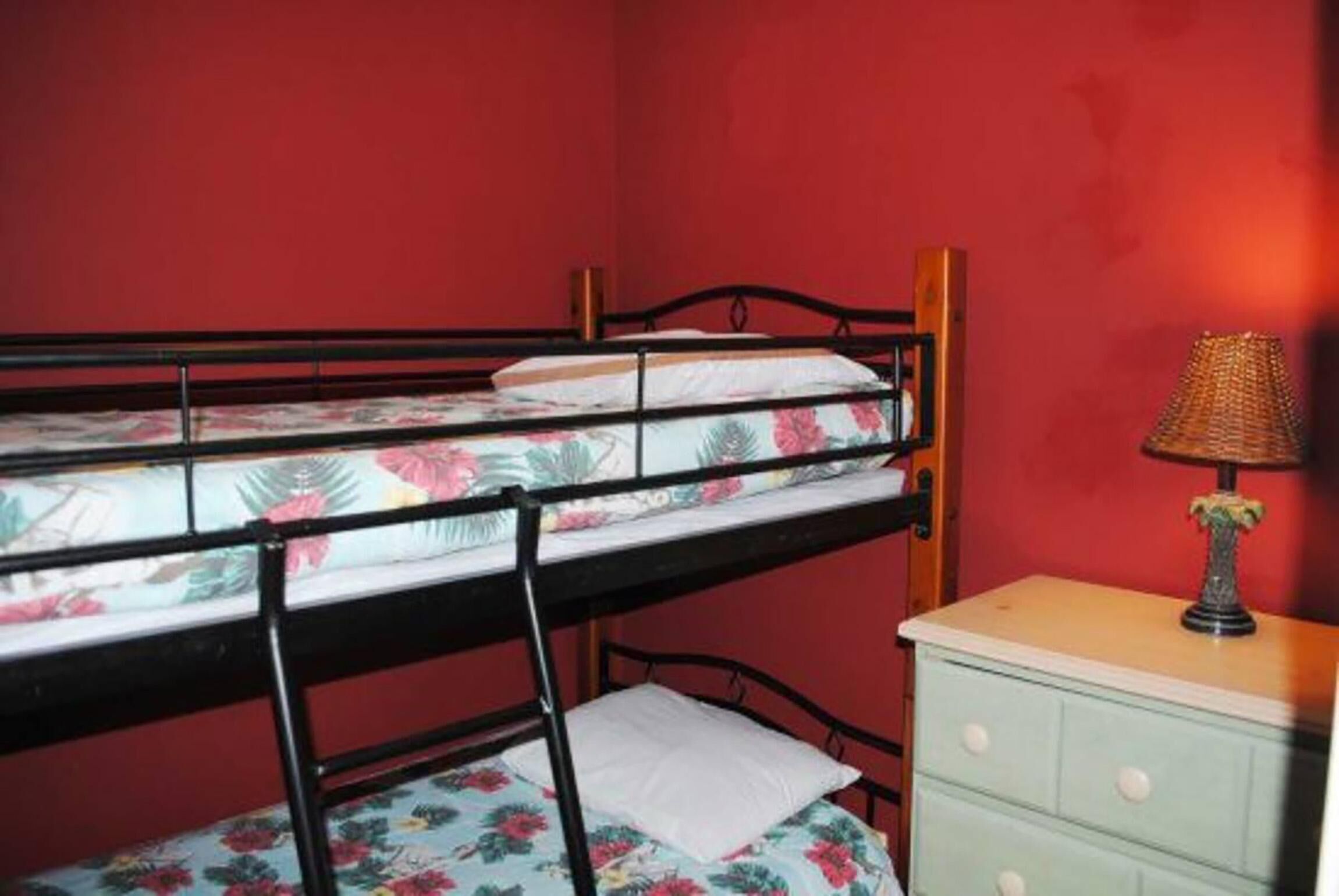 Een stapelbed met bloemenbeddengoed, een bedlampje en een klein dressoir in een kamer met rode wanden.