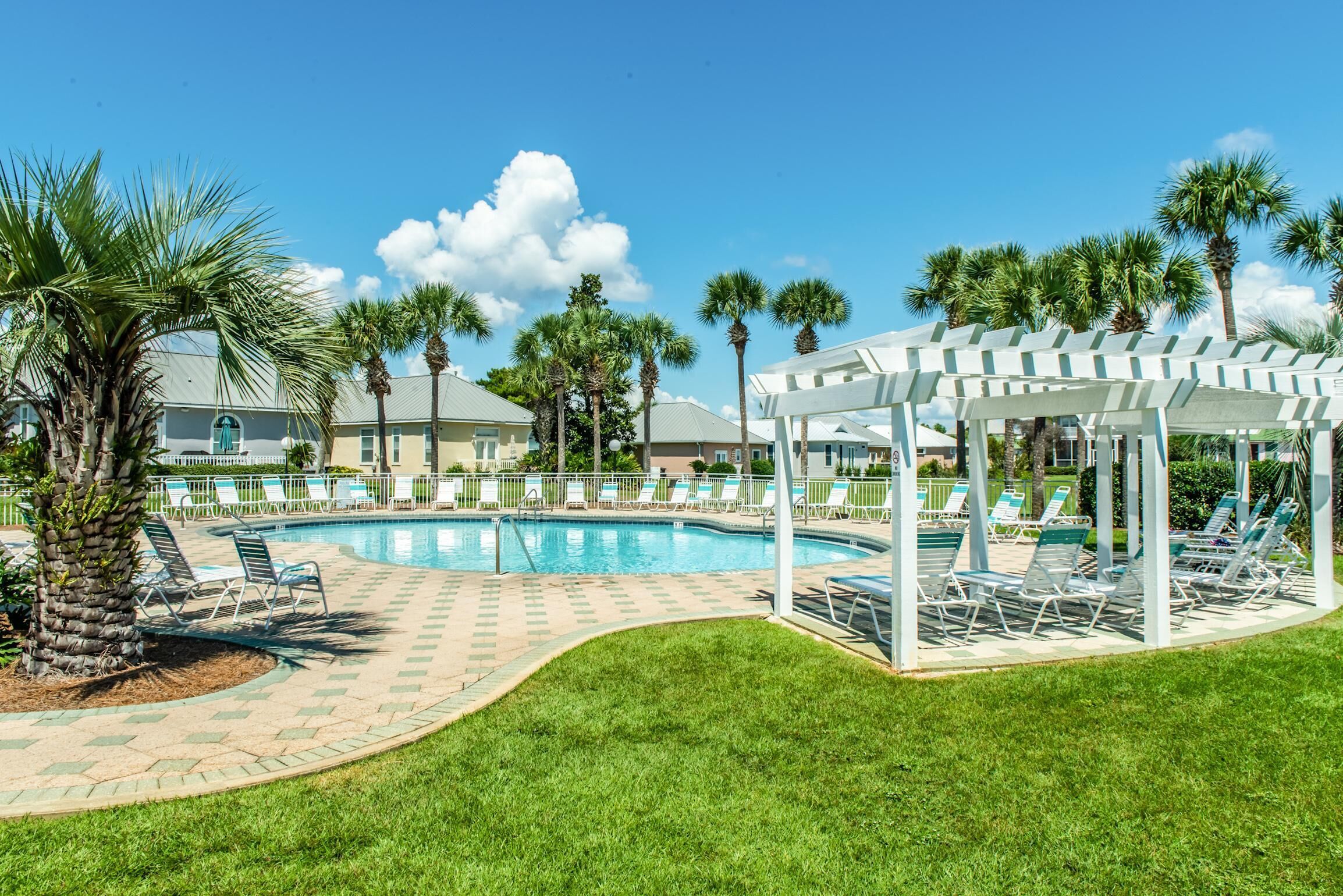 A pool area with lounge chairs, palm trees, and a covered seating area.