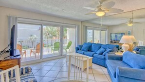 A spacious living area with a blue sofa set, a white coffee table, and a ceiling fan.