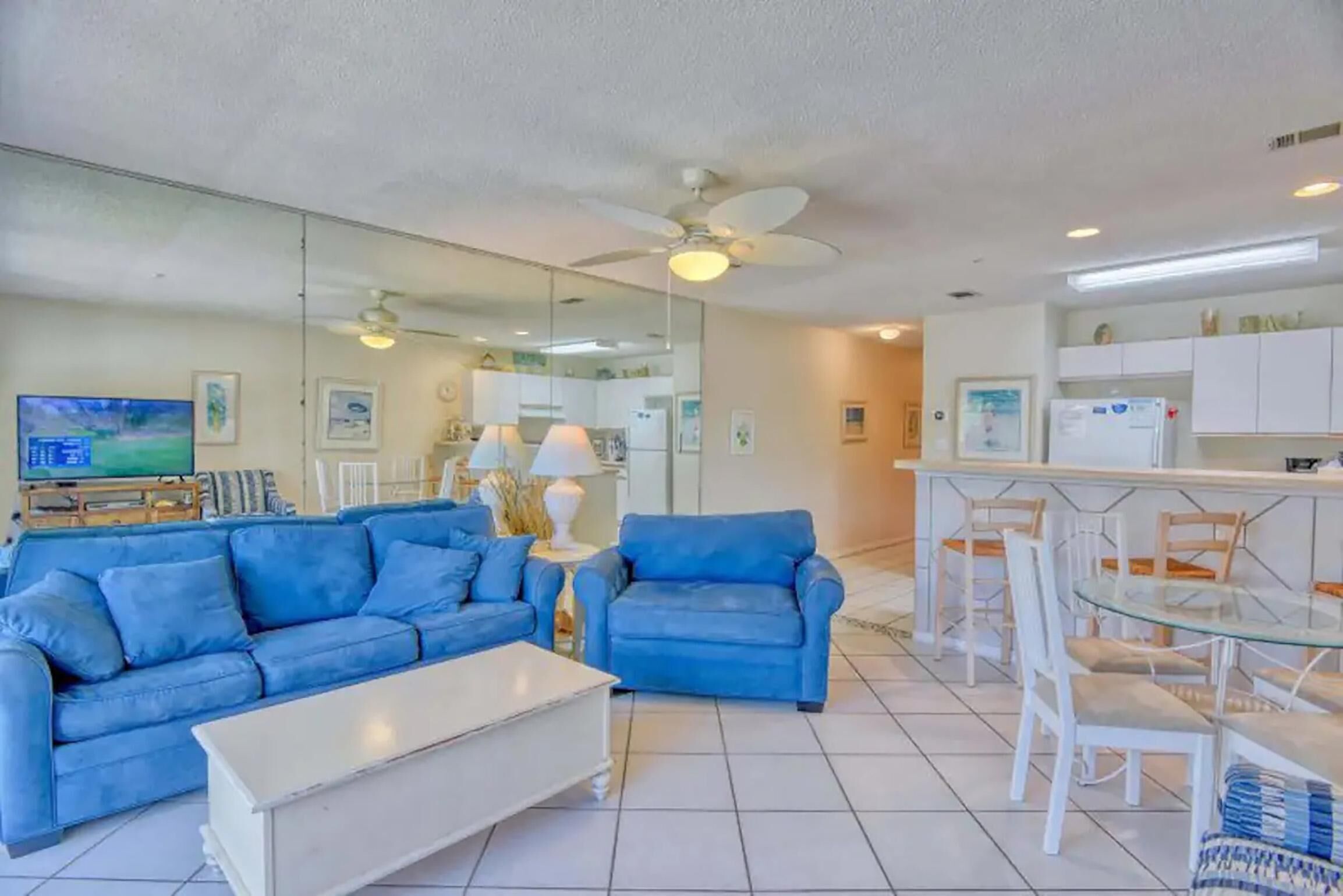 A living room with a blue sofa, a white coffee table, and a glass dining table with white chairs.