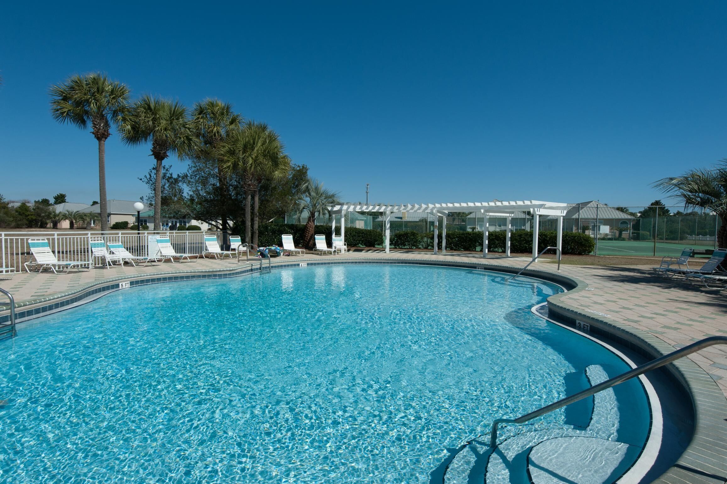 A clear blue swimming pool with lounge chairs and palm trees.
