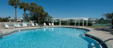 A clear blue swimming pool with lounge chairs and palm trees.
