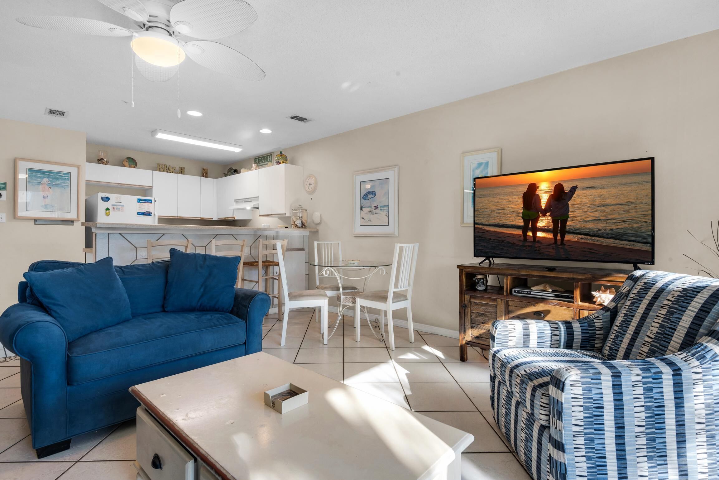 A living room with a blue sofa, a patterned sofa, a coffee table, and a TV displaying a sunset scene.