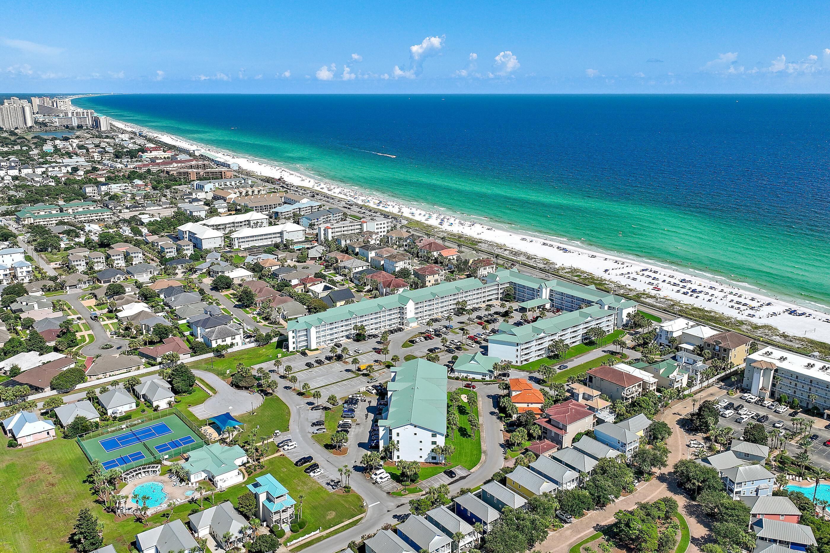 A coastal resort area with beachfront properties, a large hotel complex, and a tennis court facility.